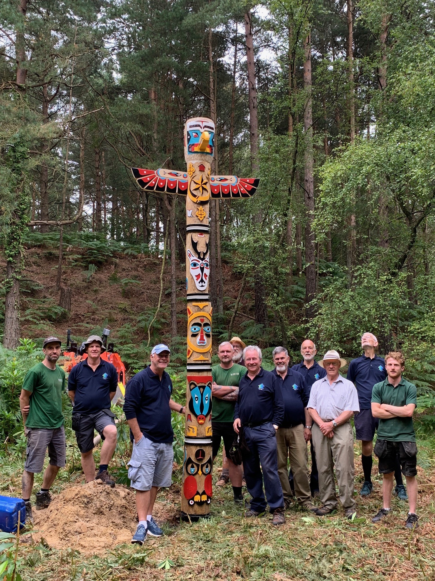 The totem pole stands proudly, surrounded by the skilled woodworkers who created it